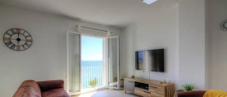 Una sala de estar con televisor, sofá, una mesa de centro y un ventanal corredizo que da a un balcón con vistas.