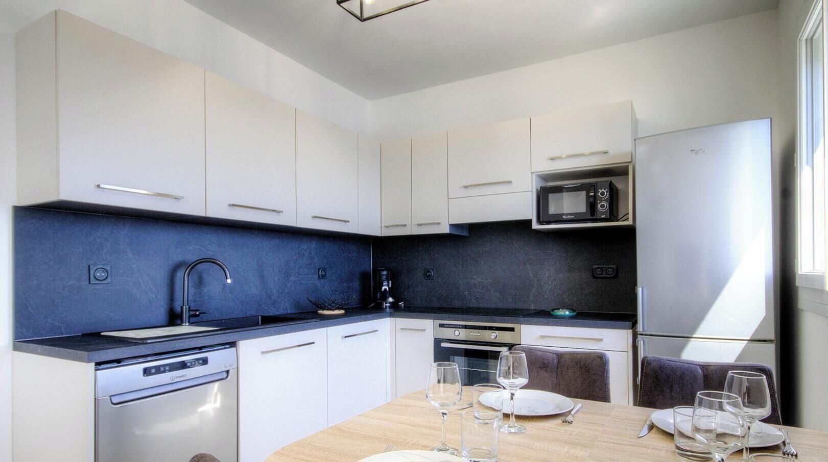 Een moderne keuken met witte kastjes, een zwart aanrecht, een ingebouwde magnetron, een oven en een eethoek met een tafel gedekt voor twee personen.