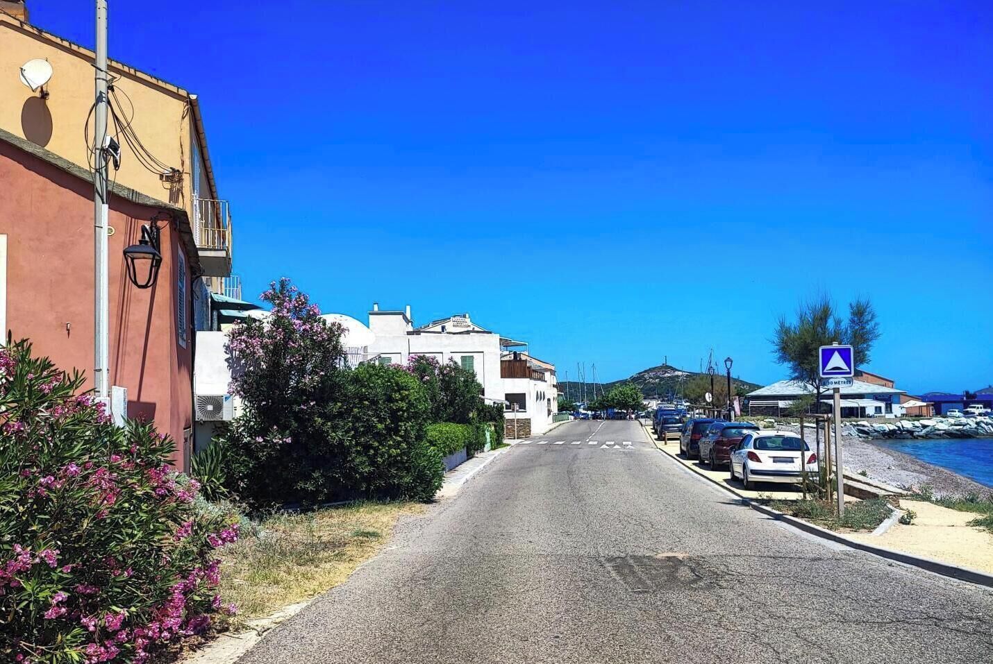 Una carretera costera con coches aparcados, un cielo azul despejado y edificios a un lado.