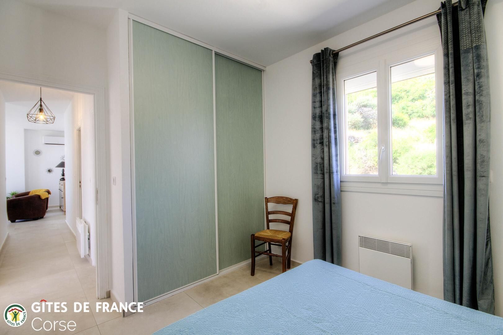 Un dormitorio con cama, una silla, una ventana con cortinas y un radiador.