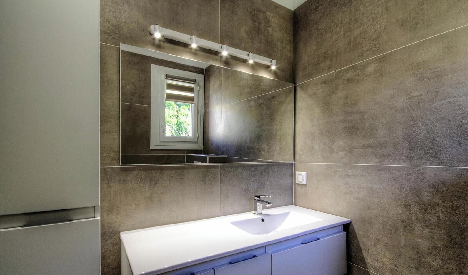 Un bany modern amb un lavabo blanc, un mirall i una finestra amb llum natural.