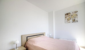 Quarto com cama, mesa de cabeceira, abajur e uma obra de arte na parede.