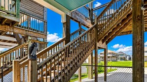 A wooden staircase with a metal railing, a concrete floor, and a chain-link fence. - Beach Access~Barefoot Bliss~Chef Kitchen~Family (Bolivar Peninsula)