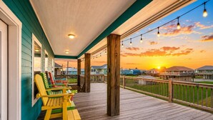 A wooden deck with chairs and a view of a sunset over a residential area. - Beach Access~Barefoot Bliss~Chef Kitchen~Family (Bolivar Peninsula)