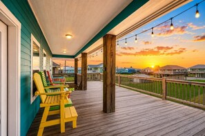 Um deck de madeira com cadeiras e vista para um pôr do sol sobre um bairro residencial.