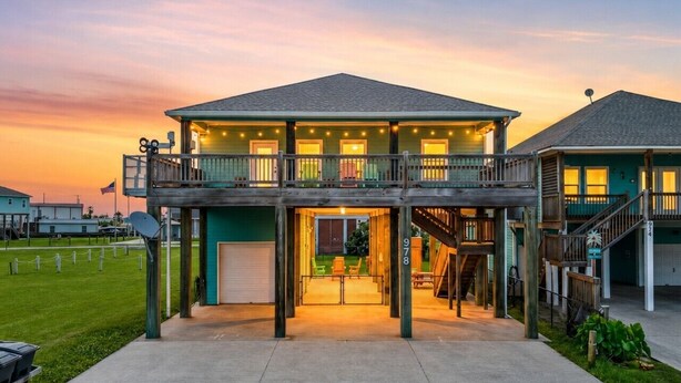 A two-story house with a balcony, a garage, and a well-maintained lawn. - Beach Access~Barefoot Bliss~Chef Kitchen~Family (Bolivar Peninsula)