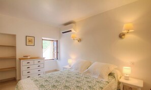 Un dormitorio con cama, lámparas de noche, ventana, cómoda y equipo de aire acondicionado.