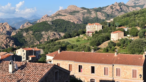 A hillside town with stone buildings, a prominent red-roofed building, and mountainous terrain in the background. - Capu D'ortu - PIANA - Gîte (PIANA)