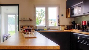 Une cuisine moderne dotée d’un îlot central, de meubles de rangement aux couleurs sombres et offrant une vue sur l’extérieur grâce à de grandes fenêtres.