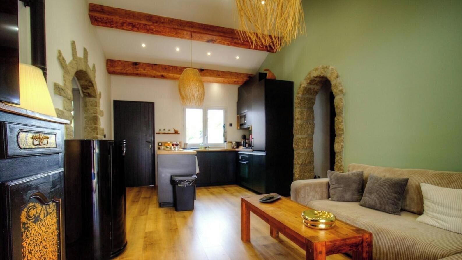 A modern kitchen with a wooden ceiling, a dining area with a wooden table, and a living room with a sofa.