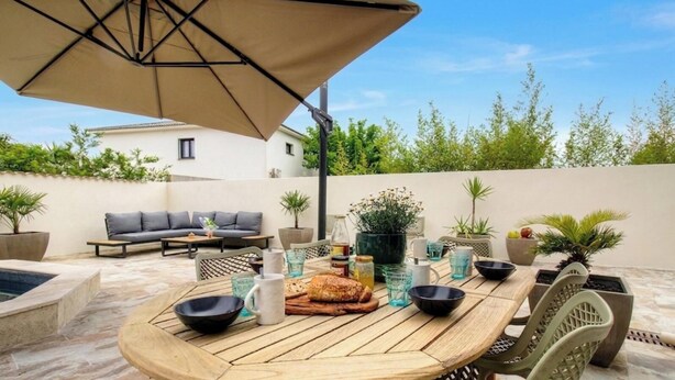 Une terrasse extérieure avec une table ronde en bois, des sièges et un grand parasol.