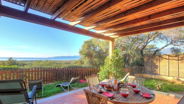Un patio al aire libre con una pérgola de madera, una mesa redonda dispuesta para comer y vistas del paisaje.