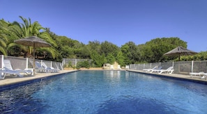 Una piscina con lettini e ombrelloni, circondata dal verde.