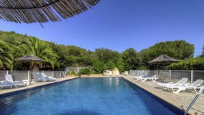 A swimming pool with white lounge chairs and thatched umbrellas, surrounded by greenery. - 10676 - SAINTE LUCIE DE PORTO VECCHIO (SAINTE LUCIE DE PORTO VECCHIO)
