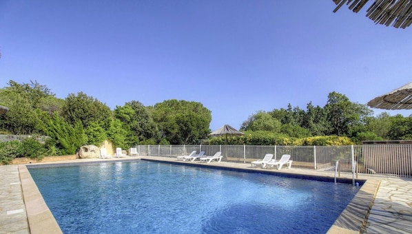 Una piscina con lettini, circondata da una recinzione e alberi.