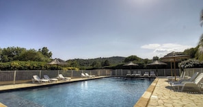 Ein Schwimmbecken mit Liegestühlen und Sonnenschirmen, umgeben von einer Hecke und Grünpflanzen.