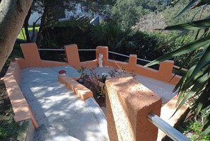 Un área de estar al aire libre con pavimento, barandilla metálica y abundante vegetación.
