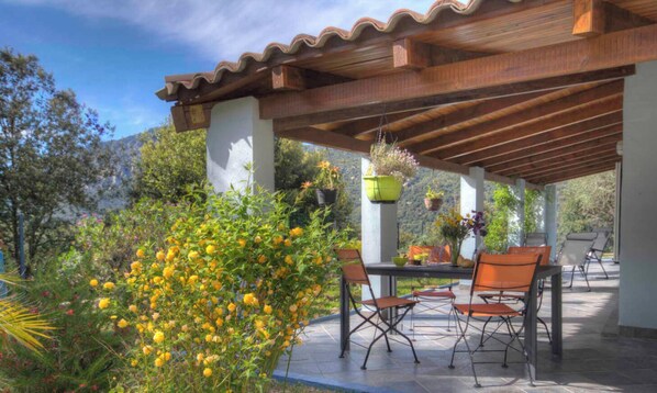 Eine Außenpatio mit einer Holz-Pergola, einem Tisch mit Stühlen und hängenden Pflanzgefäßen mit Blumen.