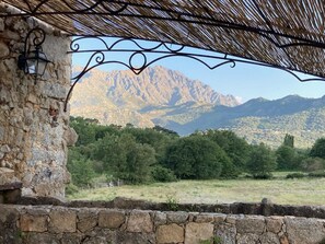 Eine Steinsäule, eine Metallpergola und eine gebirgige Landschaft.