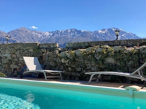 Ein Poolbereich mit Steinmauern, Liegestühlen und Blick auf die Berge.
