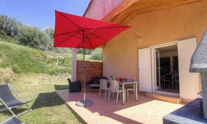 Eine Terrasse im Freien mit Tisch, Stühlen, einem roten Sonnenschirm und einem Grill.