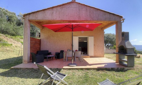 Eine überdachte Terrasse im Freien mit Sitzgelegenheiten, einem Grill und Blick auf die Landschaft.