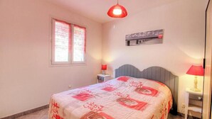 A bedroom with a bed, a window with curtains, a wall-mounted air conditioner, and a red pendant light. - Cerise - FIGARI - Gîte (FIGARI)