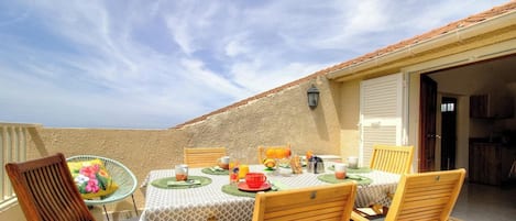 Ein Balkon mit Frühstückstisch, Stühlen und Blick aufs Meer.