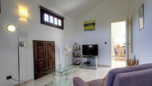A living room with a glass coffee table, a television, a fireplace, and a dining area visible through an open door. - Casa Stella Marina - SAINT FLORENT (SAINT FLORENT)