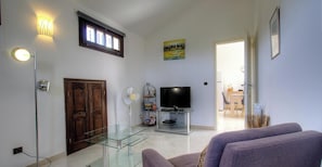 A living room with a glass coffee table, a television, a fireplace, and a dining area visible through an open door. - Casa Stella Marina - SAINT FLORENT (SAINT FLORENT)