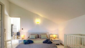 A bedroom with a bed, two bedside tables with lamps, a chair, and a crib. - Casa Stella Marina - SAINT FLORENT (SAINT FLORENT)