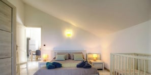 A bedroom with a bed, two bedside tables with lamps, a chair, and a crib. - Casa Stella Marina - SAINT FLORENT (SAINT FLORENT)