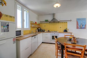 A compact kitchen with white cabinets, a microwave, a sink, and a stove. There is a dining table with chairs and a vase with flowers. - Alimea - PRUNELLI DI FIUM'ORBO (PRUNELLI DI FIUM'ORBO)