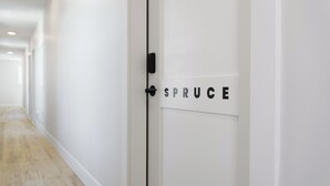 Um corredor com uma porta branca identificada com a placa 'SPRUCE'.