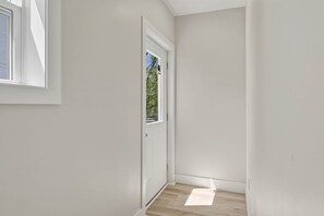 A narrow hallway with a white door, a window, and a view of trees outside. - Spruce @ Timberline Flats (Traverse City)