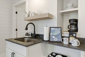 Une cuisine équipée d’un évier, d’une machine à café et d’un panneau d’accueil encadré.