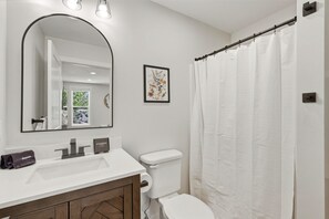 Une salle de bain avec un lavabo blanc, un miroir, des toilettes et un rideau de douche.