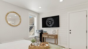 Ett sovrum med en säng, en tv, ett skrivbord, en spegel och en dörr.