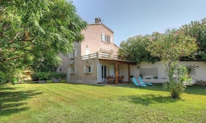 Ein zweistöckiges Haus mit Terrasse, Rasen und Baum.