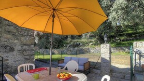 Zona esterna con posti a sedere, un tavolo, sedie, un ombrello giallo e una ciotola di frutta.