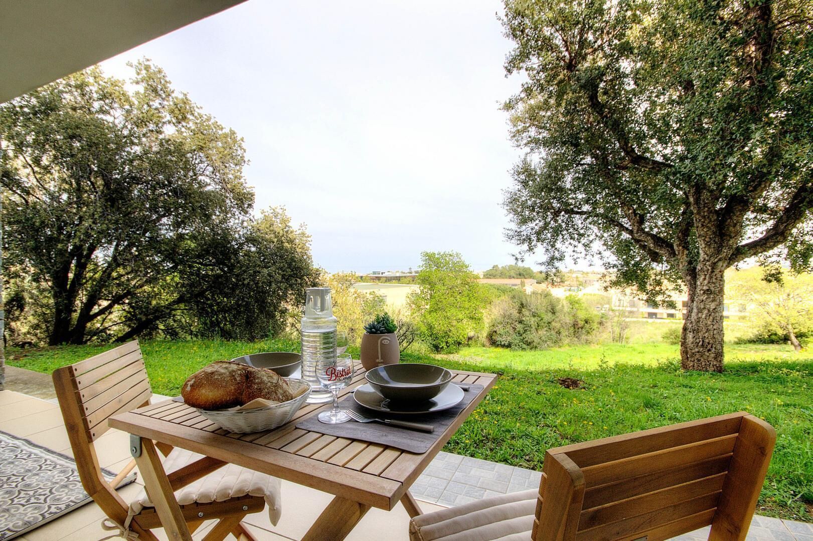 Un espacio de comedor al aire libre con una mesa preparada para dos, pan, una botella de agua y un bol.