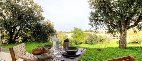 Un espacio de comedor al aire libre con una mesa preparada para dos, pan, una botella de agua y un bol.