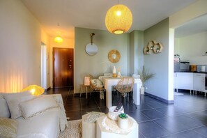 Ein modernes Wohnzimmer mit Sofa, Esstisch, Stühlen, einer Küchenzeile und einer großen Hängelampe.
