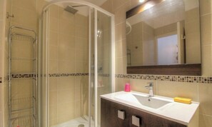Ein Badezimmer mit einer gläsernen Duschkabine, einem weißen Waschbecken mit Spiegel darüber und einer gefliesten Rückwand.