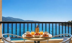 Ein Balkon mit einem Frühstückstisch, mit Blick auf ein Gewässer, auf dem Boote fahren, und Berge in der Ferne.
