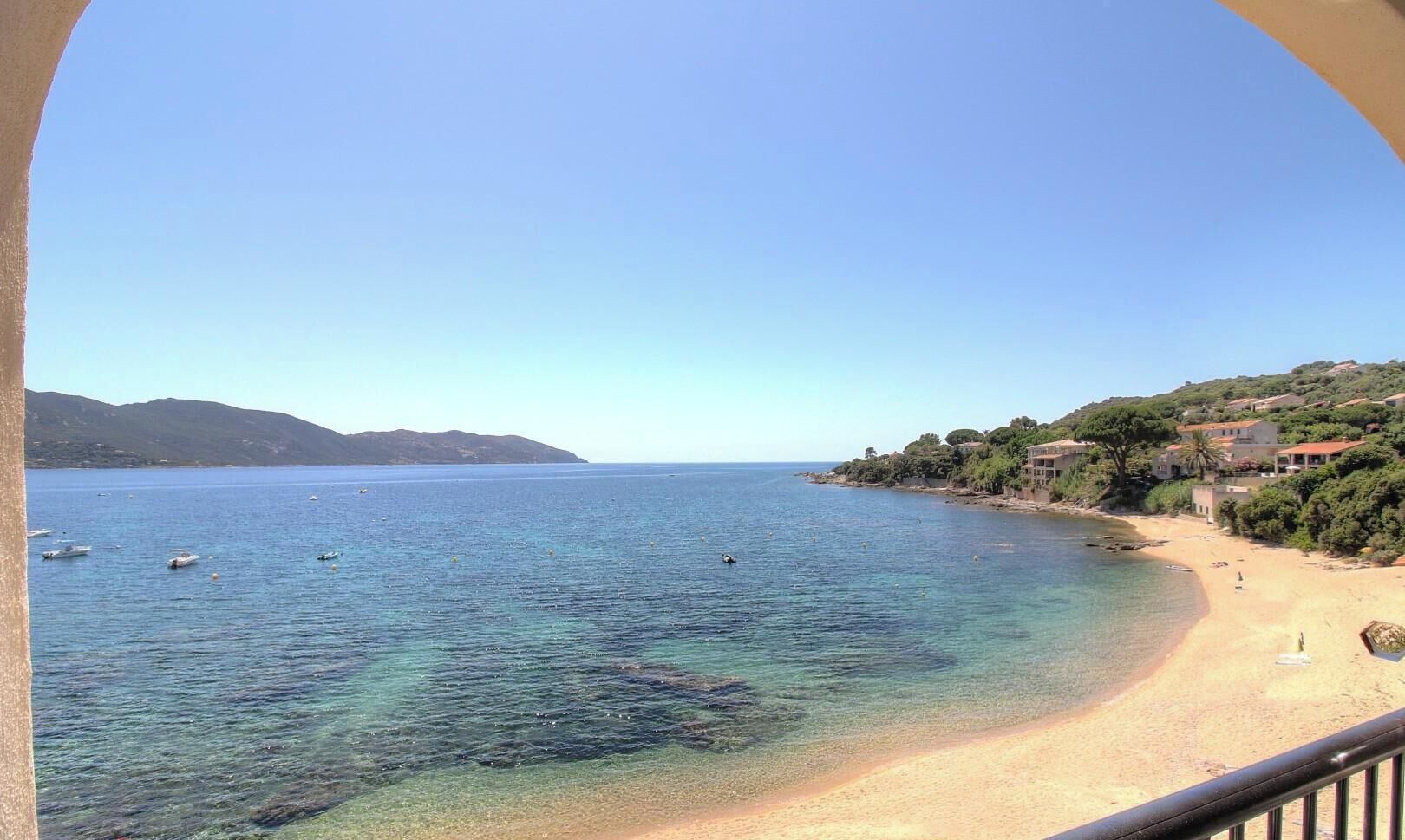 A coastal view with clear waters, a sandy beach, and buildings on a hillside.