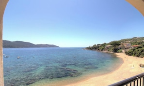 Ein Küstenblick mit klarem Wasser, einem Sandstrand und Gebäuden an einem Hügelhang.