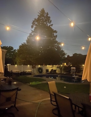 An outdoor patio area with a pool, lounge chairs, and string lights.