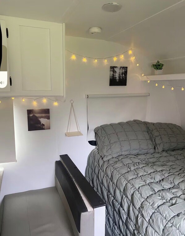 A bedroom with a bed, bedside table, hanging light string, wall-mounted shelf, and a picture.