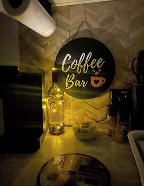 A kitchen counter with a coffee bar sign, a bottle of monogram vodka, a coffee machine, and a bowl of snacks.